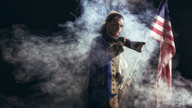 American revolution war soldier with flag of colonies and musket gun over dramatic smoke background. 4 July independence day of USA concept photo composition: soldier and flag.