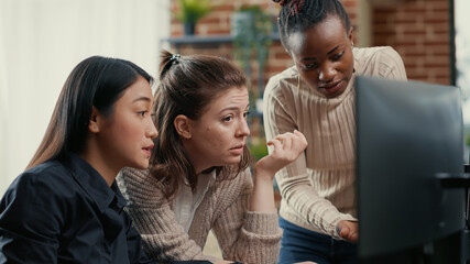 Software engineer pointing at computer screen explaining running code to coworkers brainstorming software ideas in freelance agency. Mixed team of programmers collaborating on it group project.