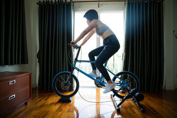 cyclist asian woman ride bicycle on trainer at home during omicron covid-19 outbreak. Stay fit and workout concept