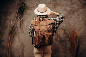 Woman with travel canvas backpack and felt hat on dark background, back view.