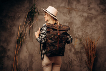 Woman with travel canvas backpack and felt hat on dark background, back view.