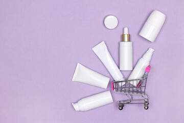 Cosmetic beauty products with shopping cart on purple background. Skin care cosmetics sale concept....