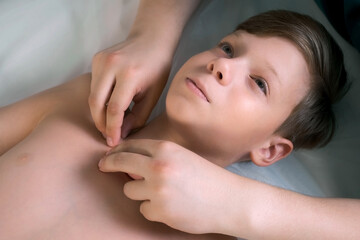 Session of craniosacral therapy, cure of teen boy spine by a doctor therapist. Boy is lying on couch. Craniosacral therapist touches boy on collarbone and shoulders to cure and correct spine posture.