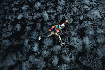 Fototapeta na wymiar a man in ice skates lies on the transparent ice of the lake, view from above, aerial photography
