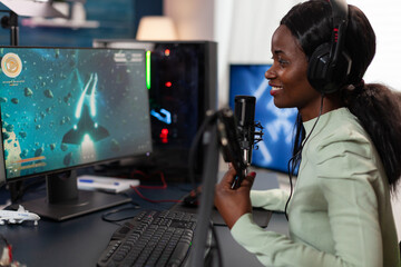 Professional woman gamer talking into microphone with players using streaming chat while playing space shooter videogames during online championship. Focused player using RBG gaming equipment