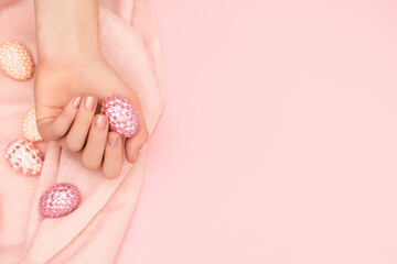 Female hand with glitter pink nail design. Female hand hold decorated easter egg. Model hand with spring nail design on pink background