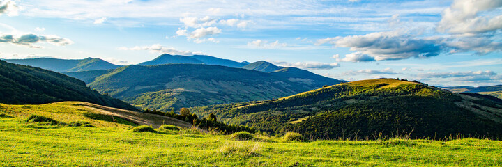 panorama landscape of mountain and green meadows at sunrise on a warm summer day. beautiful blue...