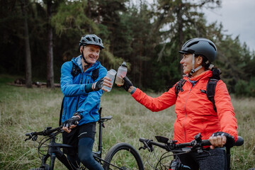 Happy senior couple bikers with water bottles outdoors in forest in autumn day.