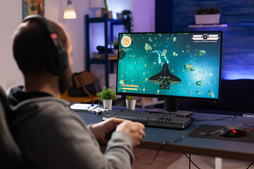 Man playing video games with controller and headphones on computer. Player using joystick and audio headset for online gaming. Gamer having fun activity with equipment to play games. © DC Studio