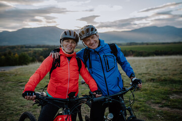 Happy senior couple bikers embracing outdoors in nature in autumn day, looking at camera.