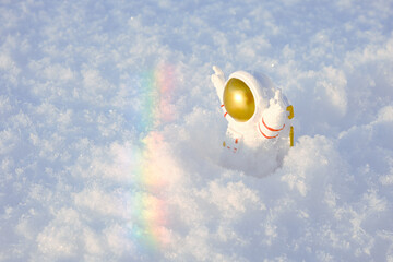 a small decorative figurine of an astronaut with his hands raised up goes through the snow to the rainbow