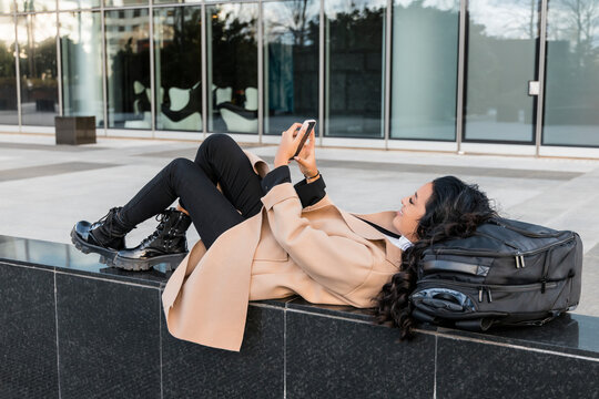 Businesswoman using smart phone lying with luggage on seat