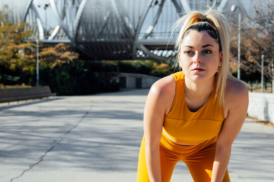 Thoughtful young sportswoman bending forward on road