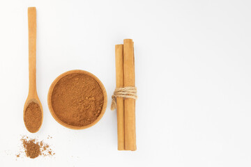 Ground cinnamon in a wooden bowl and cinnamon sticks.