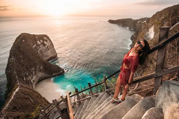 Schilderijen op glas Beautiful girl on the background of Kelingking beach, Nusa Penida Indonesia. A young woman is traveling in Indonesia. Nusa Penida is one of the most famous tourist attraction place to visit in Bali © MISHA