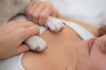 Caucasian woman lies on her back and holds a dog by the paws. 