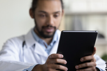 Close up focus on digital touchpad gadget in hands of young male African American general practitioner doctor physician, medical healthcare application usage, modern tech devices in telemedicine.
