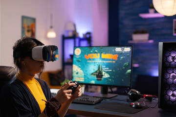 Woman winning video games with vr glasses on computer. Gamer playing with virtual reality headset and controller to win online game on monitor. Player with modern equipment at desk.