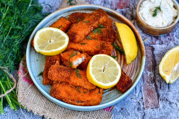Close up of   Crispy breaded  deep fried fish fingers with breadcrumbs served  with remoulade sauce and  lemon Cod Fish Nuggets on rustic wood table background