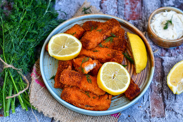 Close up of   Crispy breaded  deep fried fish fingers with breadcrumbs served  with remoulade sauce and  lemon Cod Fish Nuggets on rustic wood table background