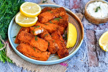 Close up of   Crispy breaded  deep fried fish fingers with breadcrumbs served  with remoulade sauce and  lemon Cod Fish Nuggets on rustic wood table background