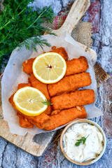 Close up of   Crispy breaded  deep fried fish fingers with breadcrumbs served  with remoulade sauce and  lemon Cod Fish Nuggets on rustic wood table background