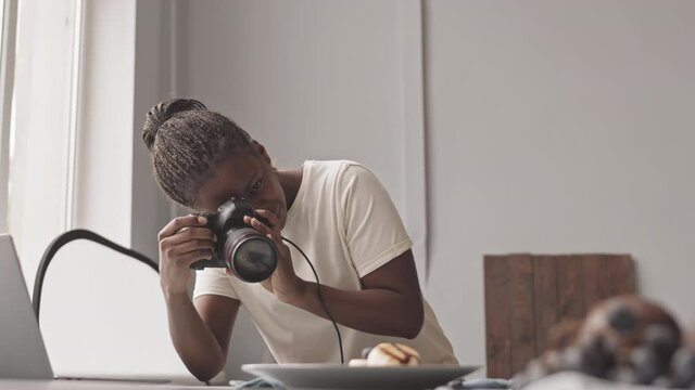 Medium slowmo shot of Black female photographer taking photos of breakfast at table on professional camera