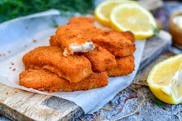 Close up of   Crispy breaded  deep fried fish fingers with breadcrumbs served  with remoulade sauce and  lemon Cod Fish Nuggets on rustic wood table background