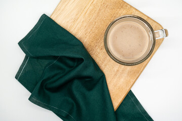 A glass cup latte placed on a wooden cutting board decorated with green cloth.