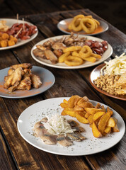 Pieces of salted herring with onions and fried potato slices in a plate and other snacks for beer from fish and meat on a wooden table. Vertical orientation, no people