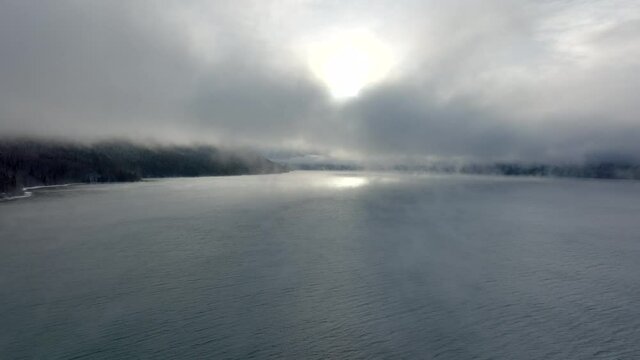 Aerial tracking across Kenai Lake during sunrise while the sun peaks through the thick low clouds on a beautiful Alaska Winter morning