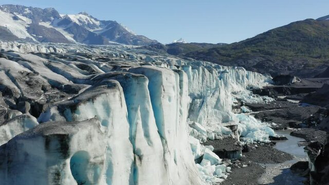 Aerial orbit reveal of Knik Glacier in Alaska. This breathtaking view shows the stark contrast of a frozen tundra to a lush green landscape.