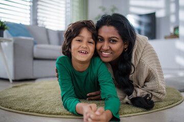 Indian mother lying on floor with her little son at home, looking at camera.