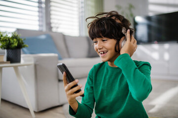 Happy multiracial boy with headphones and smartphone listening to music at home.