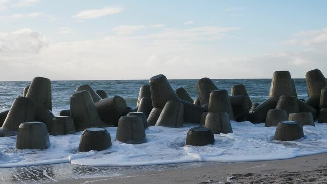On a sunny day at the beach of Hörnum waves are hitting tetrapods in slow motion. The concrete blocks protect the coast and beach of the island Sylt from the elements of the North Sea.