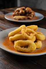 Beer appetizer assorted barbecue squid rings in batter, chicken wings in a plate on a wooden table. Vertical orientation, close-up, dark moody
