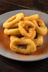 Beer appetizer from squid rings in batter in a plate on a wooden table. Vertical orientation, close-up, dark moody