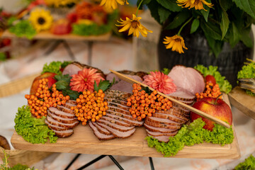 In autumn style , wooden tray with сold meat snacks is decorated and served with clusters of mountain ash on buffet table inrestaurant hall forfestive event . Recreation and entertainment.