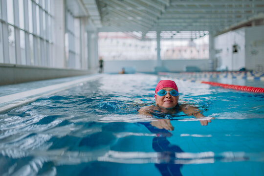 Active senior woman swimming in indoors swimming pool.