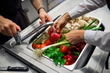 Close-up of cook washing vegetables in sink in commercial kitchen.