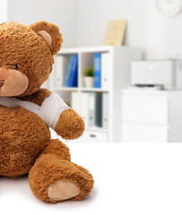 medicine, healthcare and childhood concept - teddy bear toy with bandaged paw over medical office at hospital background
