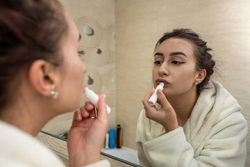 beautiful young girl in a white coat makes a boring makeup to a spacious mirror.