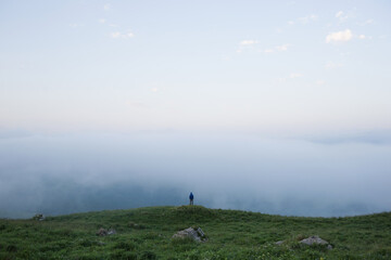 Tiny Human in mountainous area against background of field of grass and clouds. man alone with nature. little man in big world