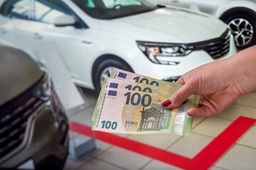  female hand with manicured red nails holds a large amount of euro banknotes near the car