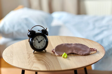 bedtime and morning concept - close up of alarm clock, earplugs and eye sleeping mask on night table at home