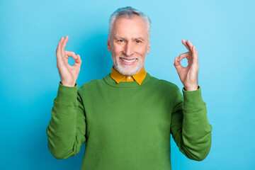 Fototapeta Photo of pretty handsome retired man wear green sweater showing two okey gestures isolated blue color background obraz