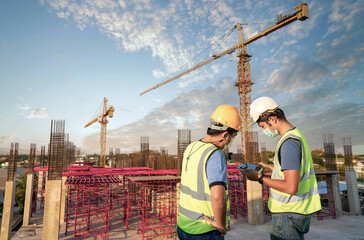 Couble male engineers dressed in work vests and hard hats for safety action plan and discuss the construction process with tablet under construction.young man working in building construction side