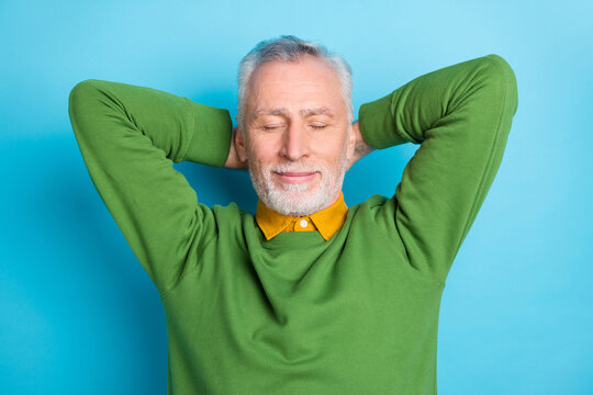Photo of pretty dreamy retired man wear green sweater closed eyes arms behind head isolated blue color background