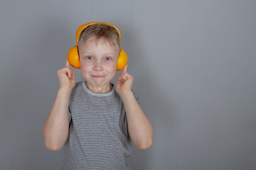 A blond 7 old Caucasian boy in a gray T-shirt and orange headphones made of oranges is playing...