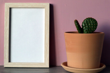 Mock up white frame with clay flower pot with cactus on pink background.